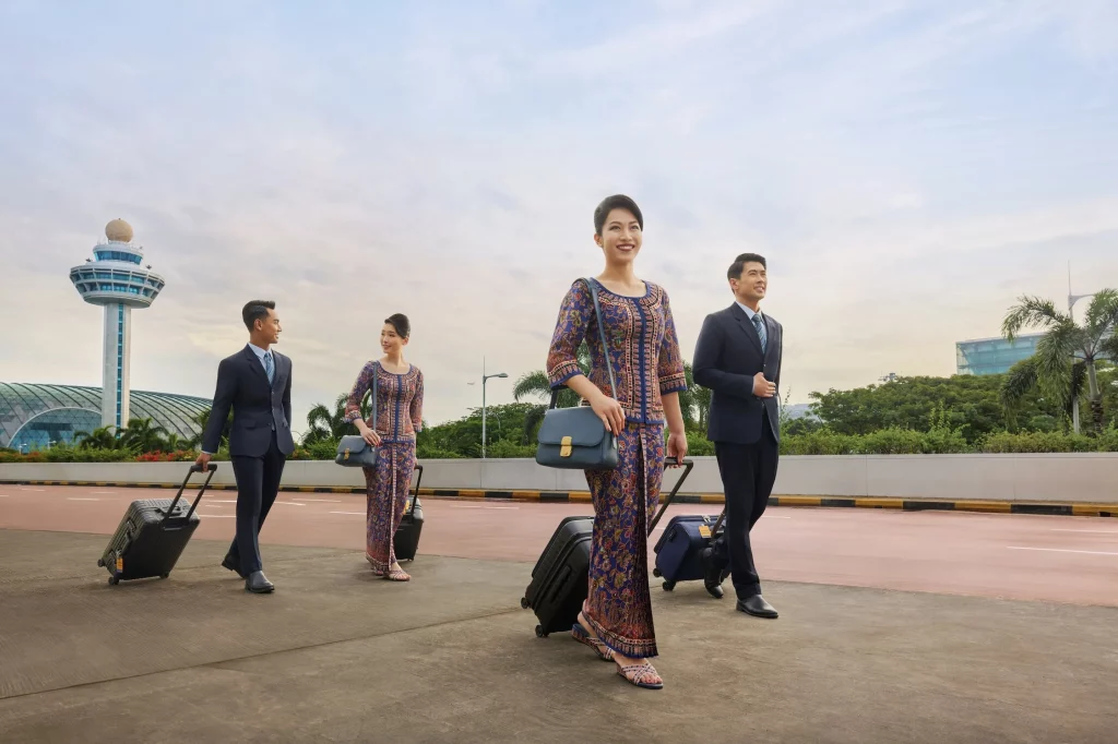 comissários de bordo da Singapore Airlines uniformizados, sendo duas mulheres vestindo o sarong kebaya em batik na cor azul e dois homem de terno
