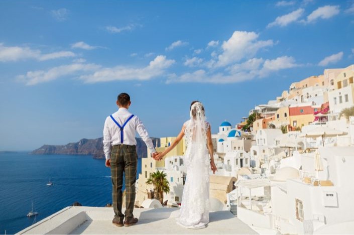 noivos de costas em roupas de casamento olhando para o mar azul
 