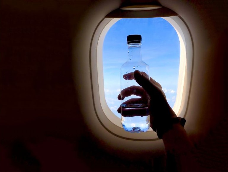 Garrafa de água erguida na frente da janela do avião